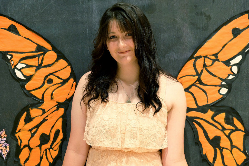 Graduate Amber poses in front of monarch butterfly wings